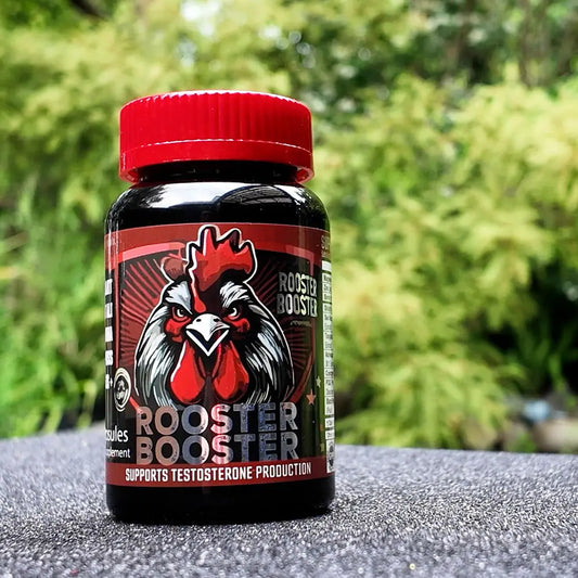 Rooster Booster supplement bottle with a red cap on a textured surface with green foliage in the background